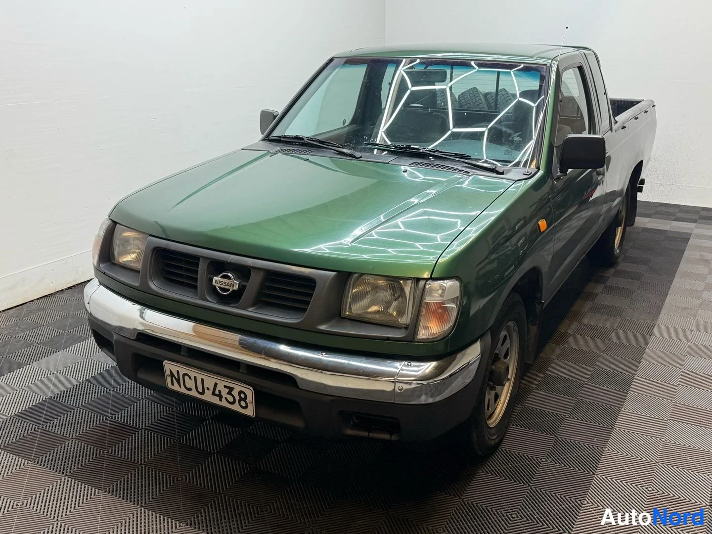 Etuviisto, nokka vasemmalle: Vihreä Nissan-pickup korkealta etukulmasta vasemmalle; etusäleikössä Nissan-merkki ja rekisterikilpi.