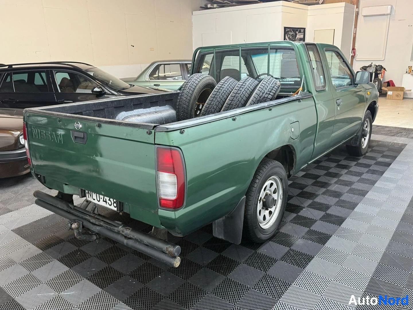 Takaviisto: Vihreä Nissan-lavamalli takaapäin, Nissan-teksti avolavassa, kilpi ja vetokoukku.