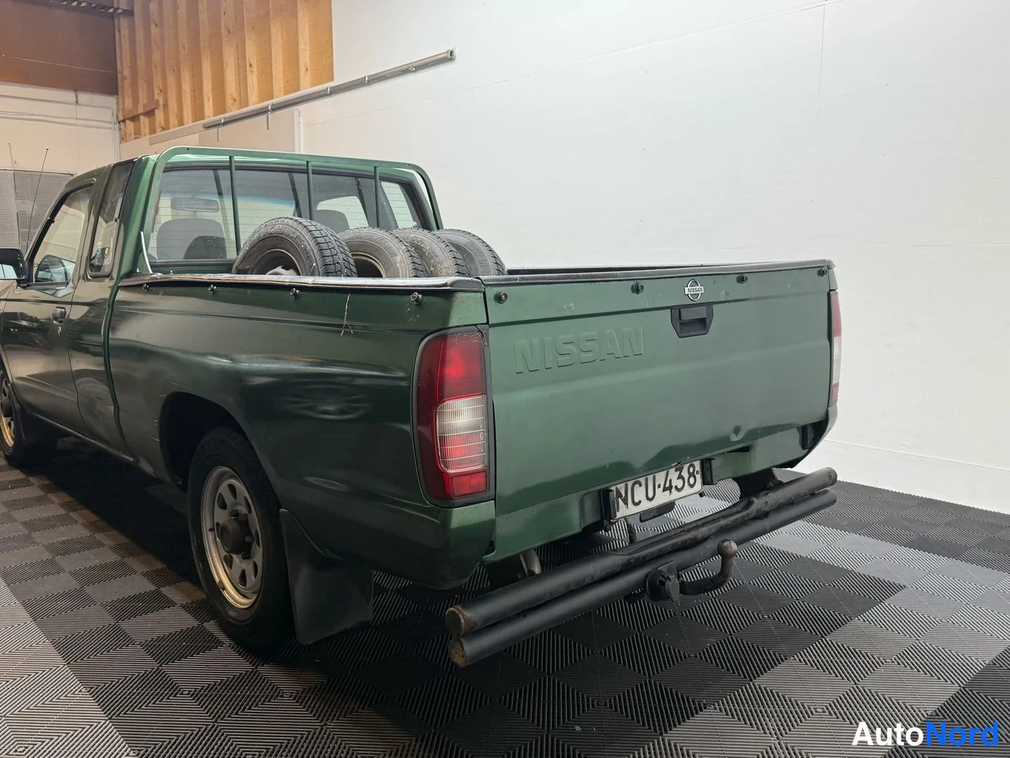 Takaviisto: Vihreä avolava-auto takaa- ja sivulta kuvattuna, lavassa renkaita, rekisteri, takana vetokoulu.