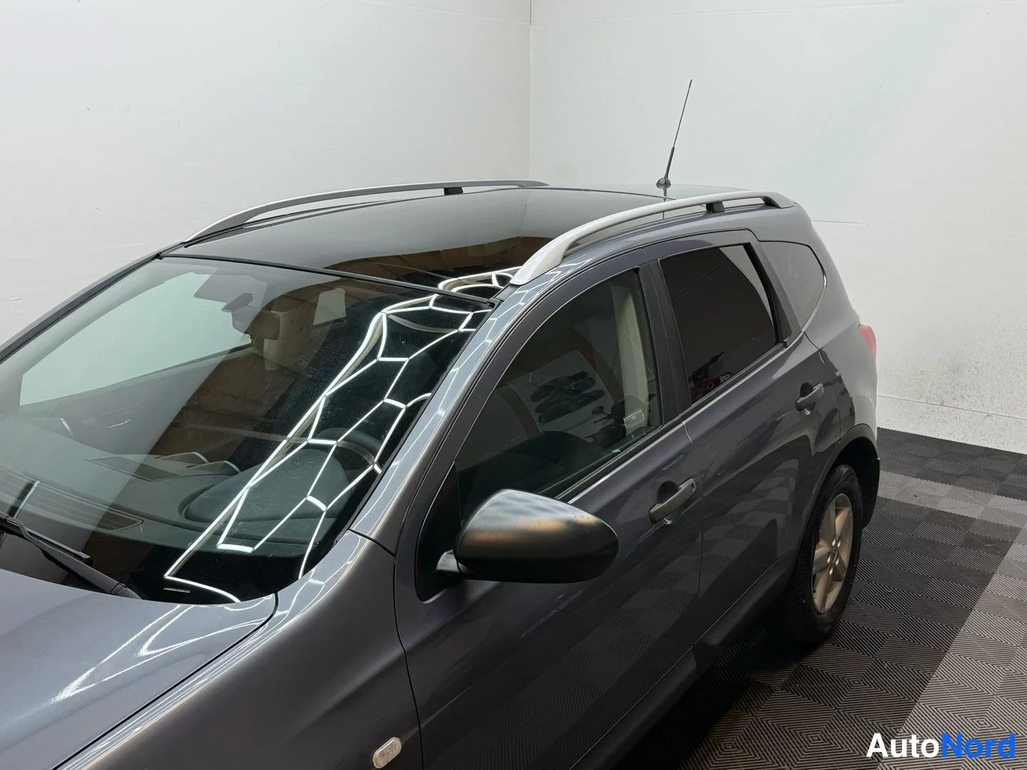 Sivulta: Harmaa Nissan Qashqai +2 yläviistosta sivulta; panoramakatto, kattokaiteet ja sivupeili näkyvissä.