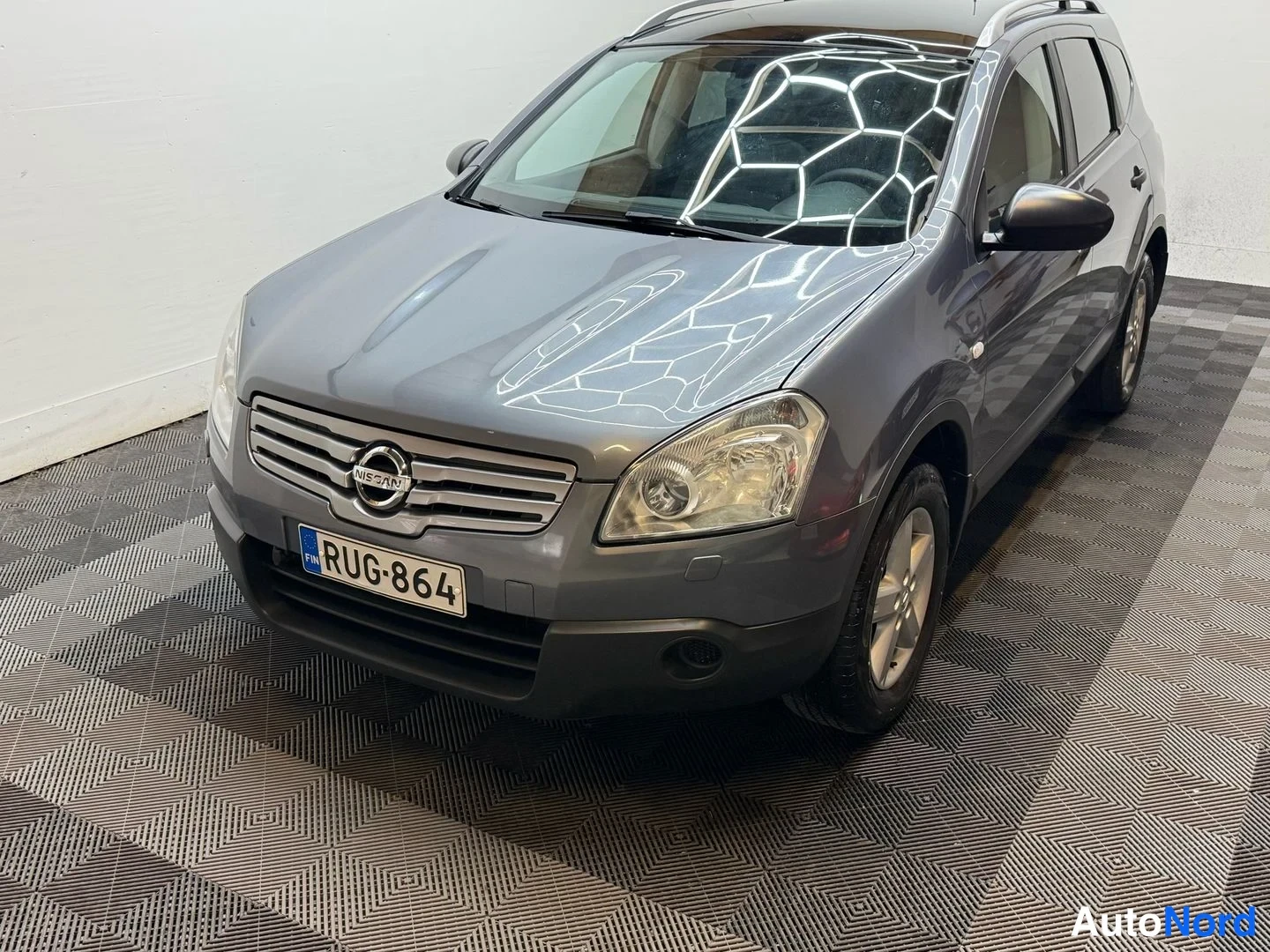 Etuviisto, nokka vasemmalle: Auton keula yläviistosta: tummanharmaa Nissan Qashqai rekisteritunnuksella, etusäleikkö, ajovalot ja konepelti näkyvissä.