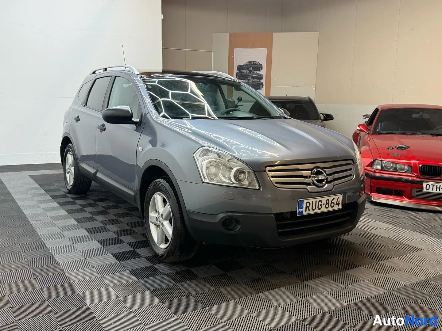 Etuviisto, nokka oikealle: Nissan Qashqai+2 kolmivartalokulmassa edestä oikealta, harmaa, kattotelineet, rekisterikilpi.