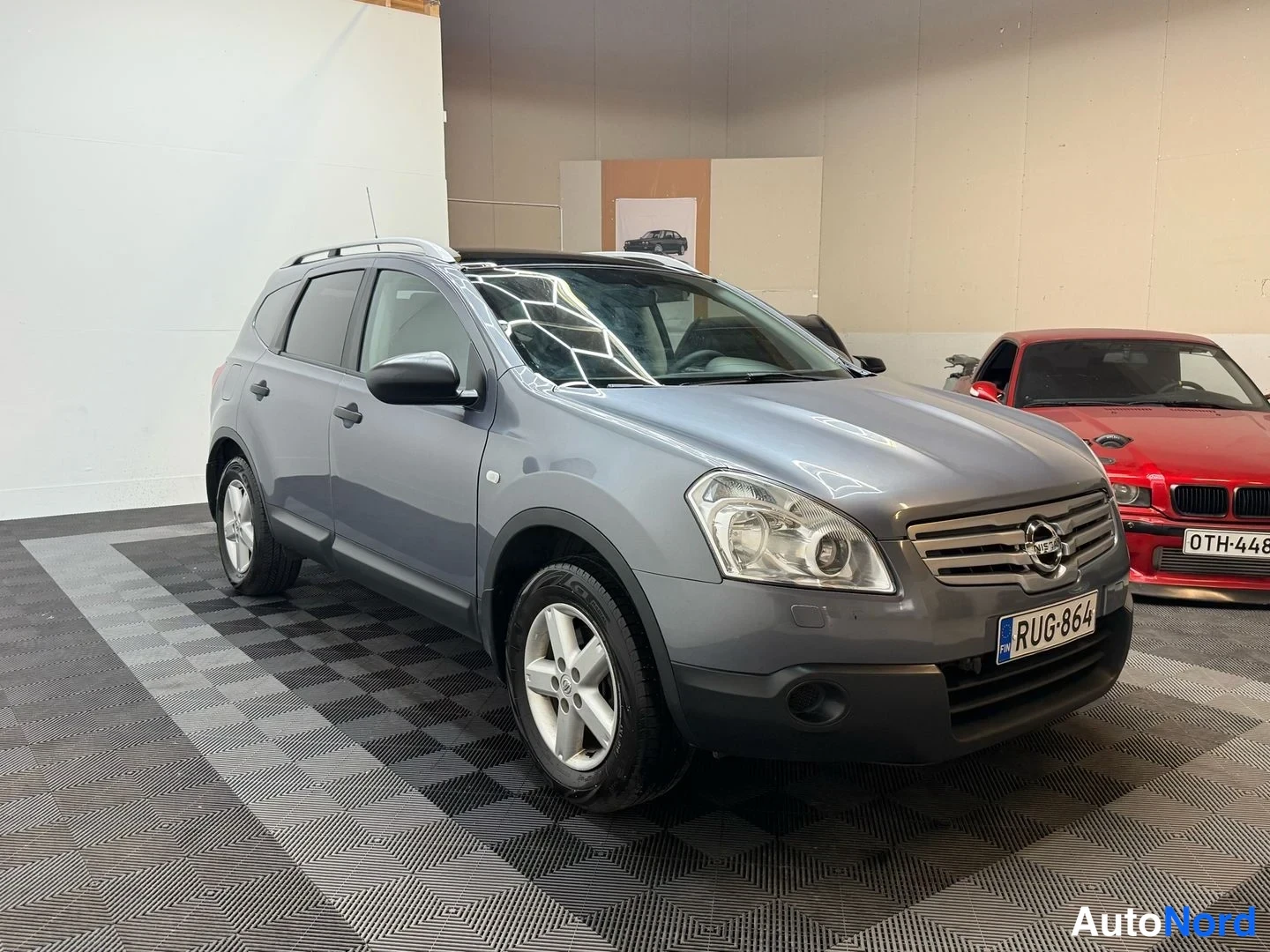 Etuviisto, nokka oikealle: Nissan Qashqai+2 kolmivartalokulmassa edestä oikealta, harmaa, kattotelineet, rekisterikilpi.