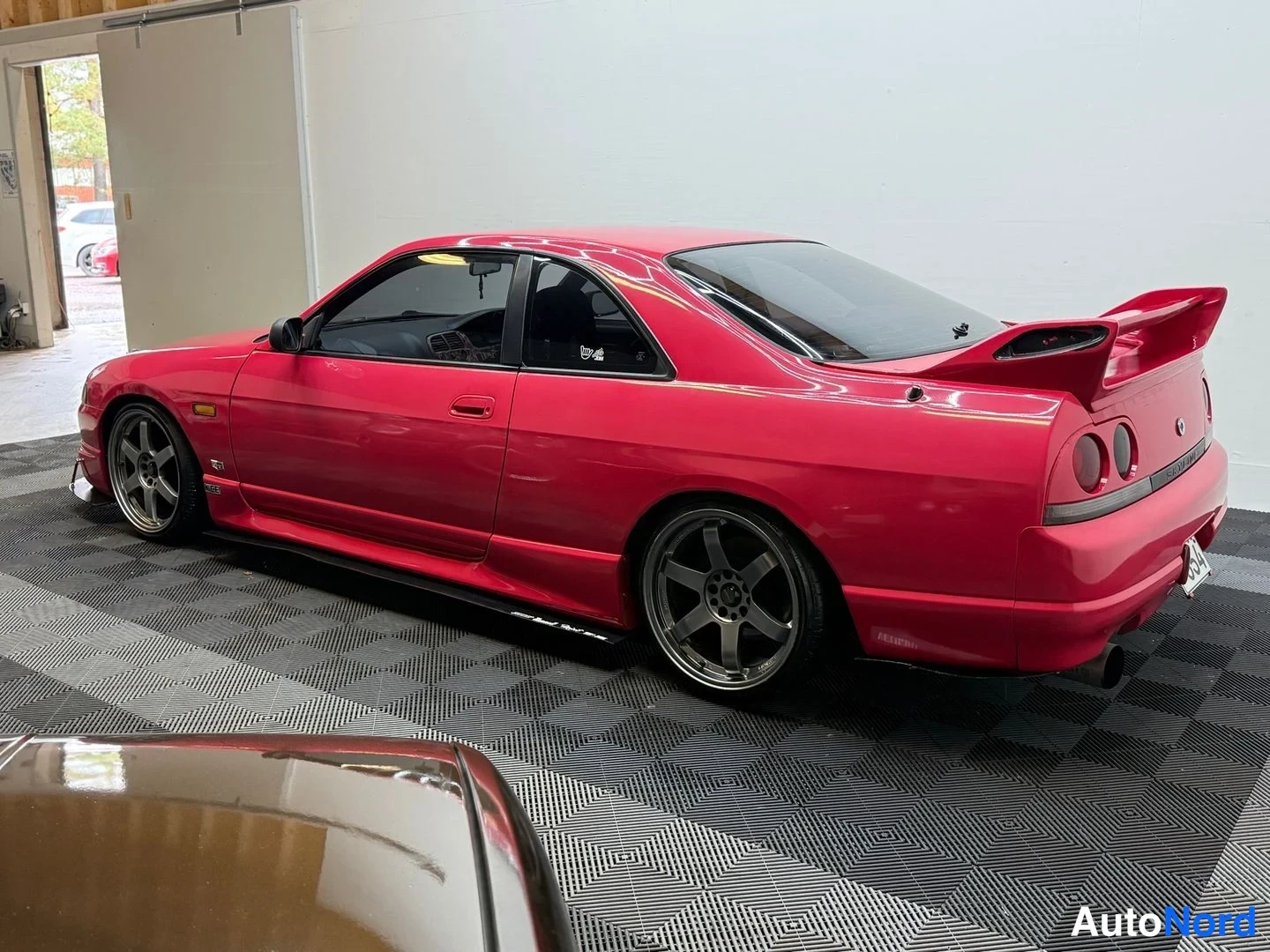 Etuviisto, nokka vasemmalle: Punaisen Nissan Skyline -auton etukulma sisätiloissa, vasen sivu ja nokka näkyvissä.