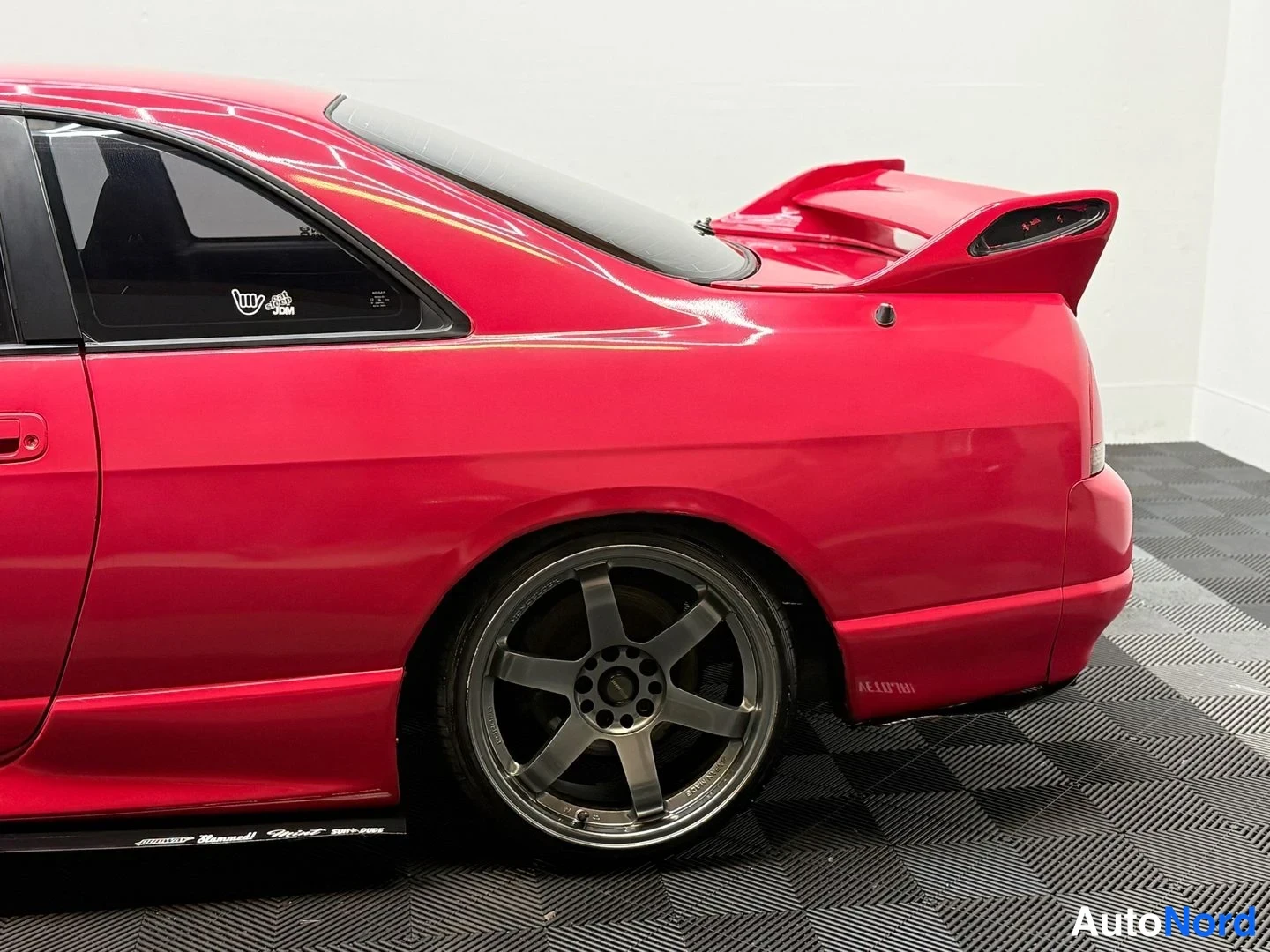 Takaviisto: Punaisen Nissan Skyline -coupén takaosa ja sivuprofiili; kakkospakoputki, suuri takasiipi ja tummat kevytmetallivanteet näkyvät.