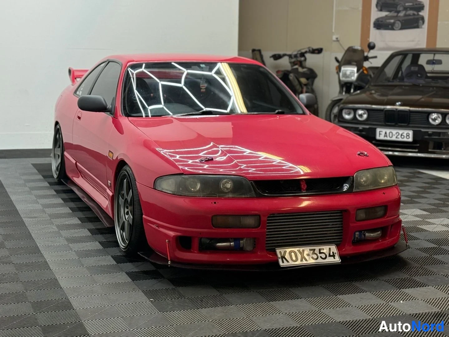 Etuviisto, nokka oikealle: Punainen Nissan Skyline kolmasosa­kuvassa keulan osoittaessa oikealle; spoileri, kevytmetallivanteet ja etumoottorin välijäähdytin näkyvät.