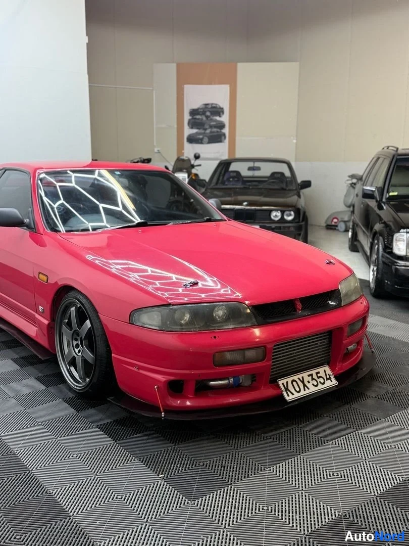 Etuviisto, nokka oikealle: Punainen Nissan Skyline kolmasosa­kuvassa keulan osoittaessa oikealle; välijäähdytin, mustat vanteet ja spoileri näkyvät.