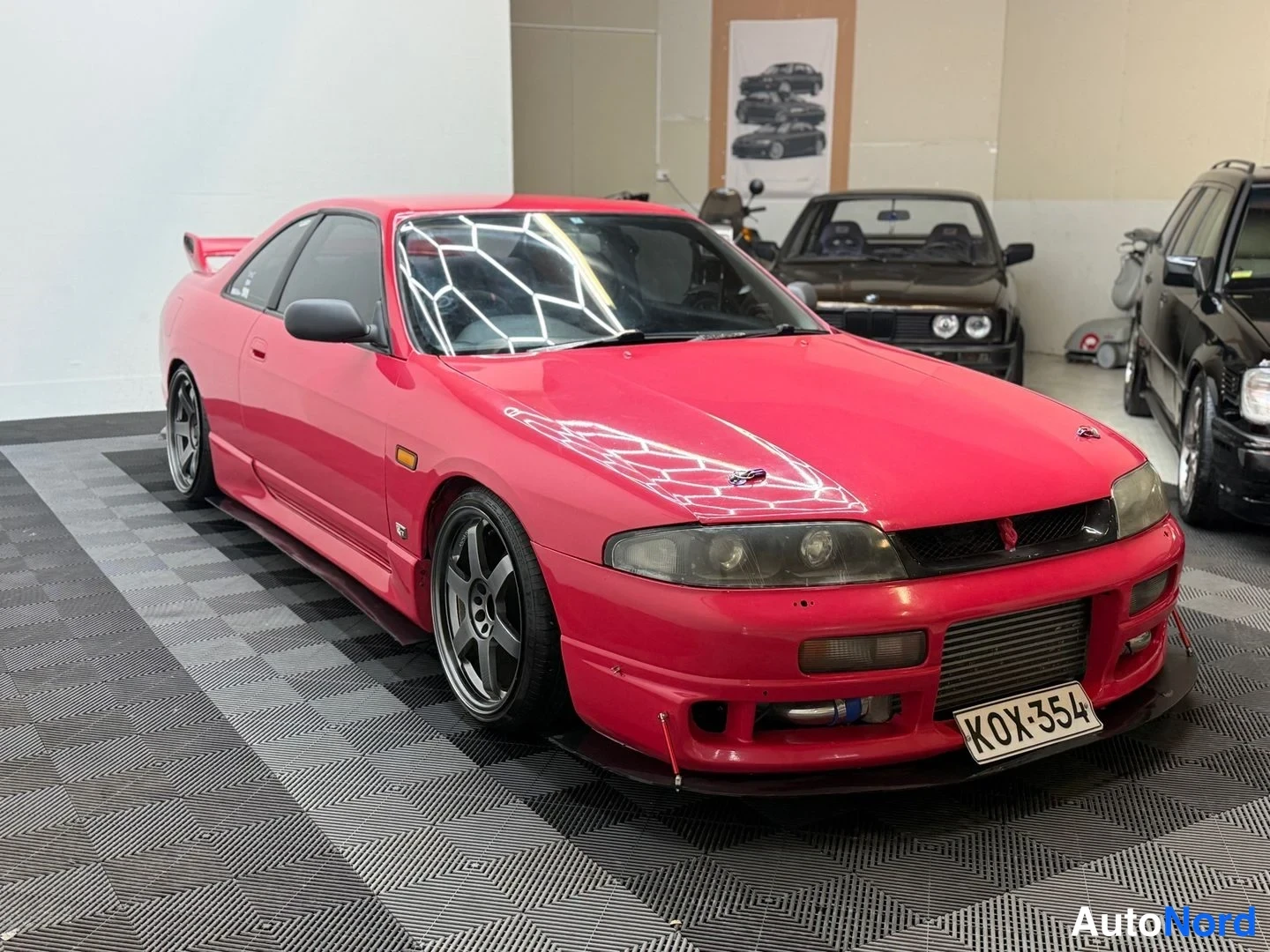 Etuviisto, nokka oikealle: Punainen Nissan Skyline kokonaisuudessaan kolmasosa­kuvassa keulan osoittaessa oikealle; spoileri, välijäähdytin ja vanteet näkyvät.