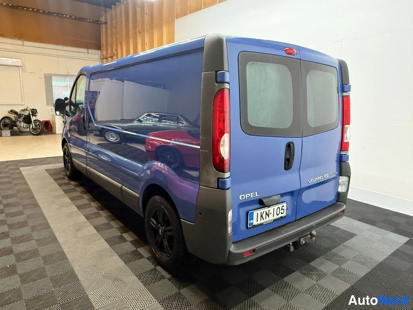 Takaviisto: Sininen Opel Vivaro -pakettiauto takaa ja vasenta sivua näkyvästi autotallissa; rekisterikilpi, OPEL- ja VIVARO CDTI -tunnukset.