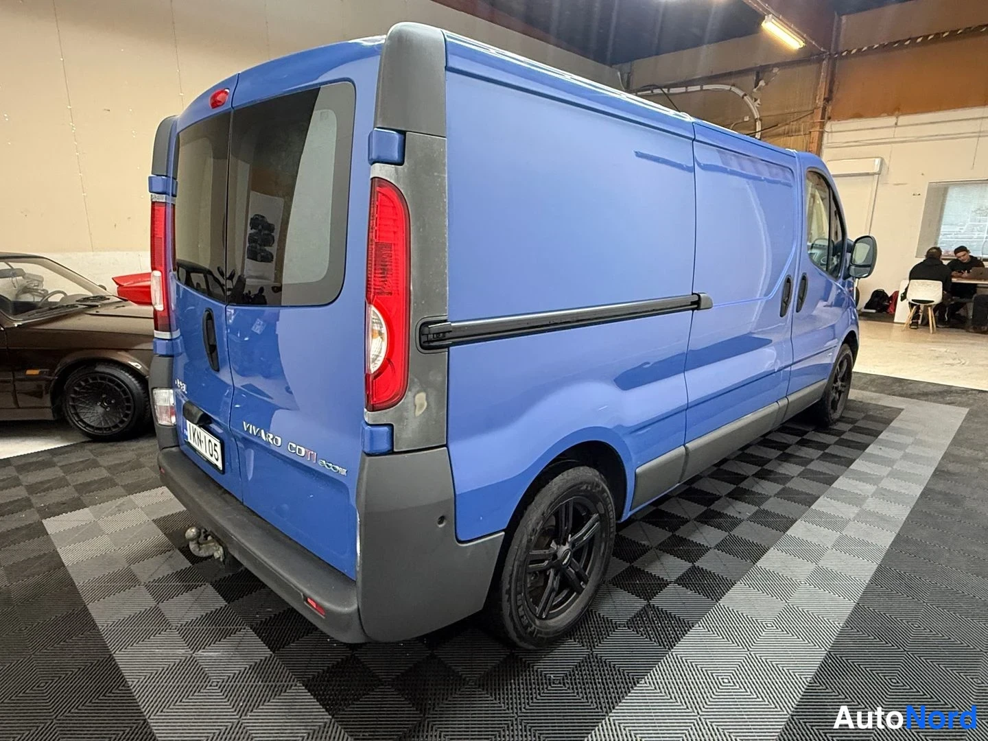Takaviisto: Sininen Opel Vivaro -pakettiauto takaa ja vasenta kylkeä päin hallissa; pitkä akseliväli, rekisterikilpi ja Vivaro CDTI ecoFLEX -teksti.