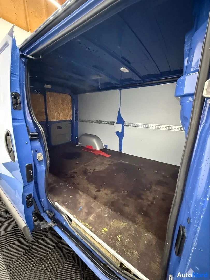 Muu: Sininen pakettiauto sisäpuolelta: pitkä tyhjä lastitila, jonka lattialla tumma matto ja sivuseinät peitettyjä.