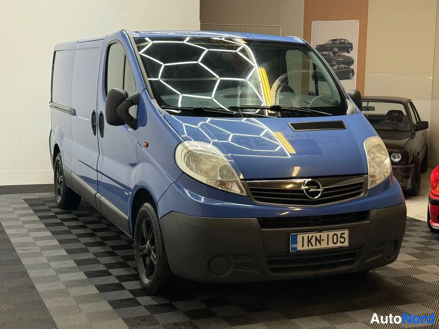 Etuviisto, nokka oikealle: Sininen Opel Vivaro -pakettiauto etukulmasta oikealta, rekisterikilpi.