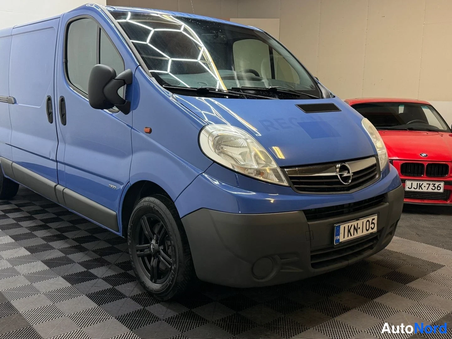 Etuviisto, nokka oikealle: Sininen Opel-pakettiauto kuvattu etukulmasta, keula oikealla; rekisterikilpi.
