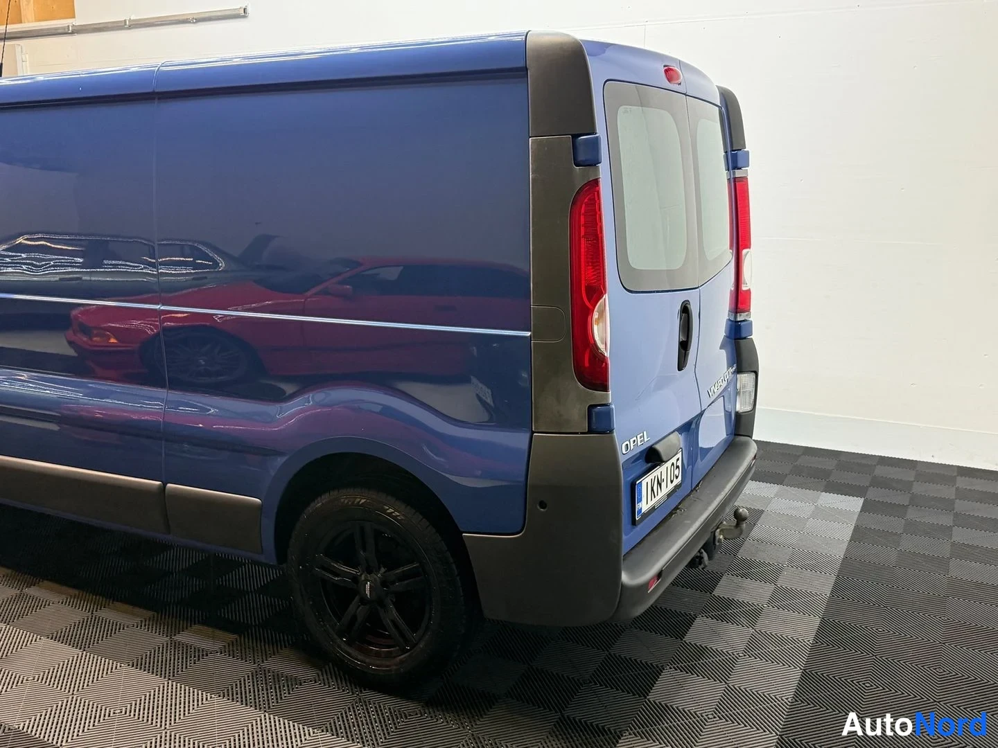 Takaviisto: Sininen Opel Vivaro -pakettiauto takaa kolmannelta neljännekseltä; takavalo, OPEL-tunnus, rekisterikilpi ja musta keulaonenä näkyvät sisätiloissa.