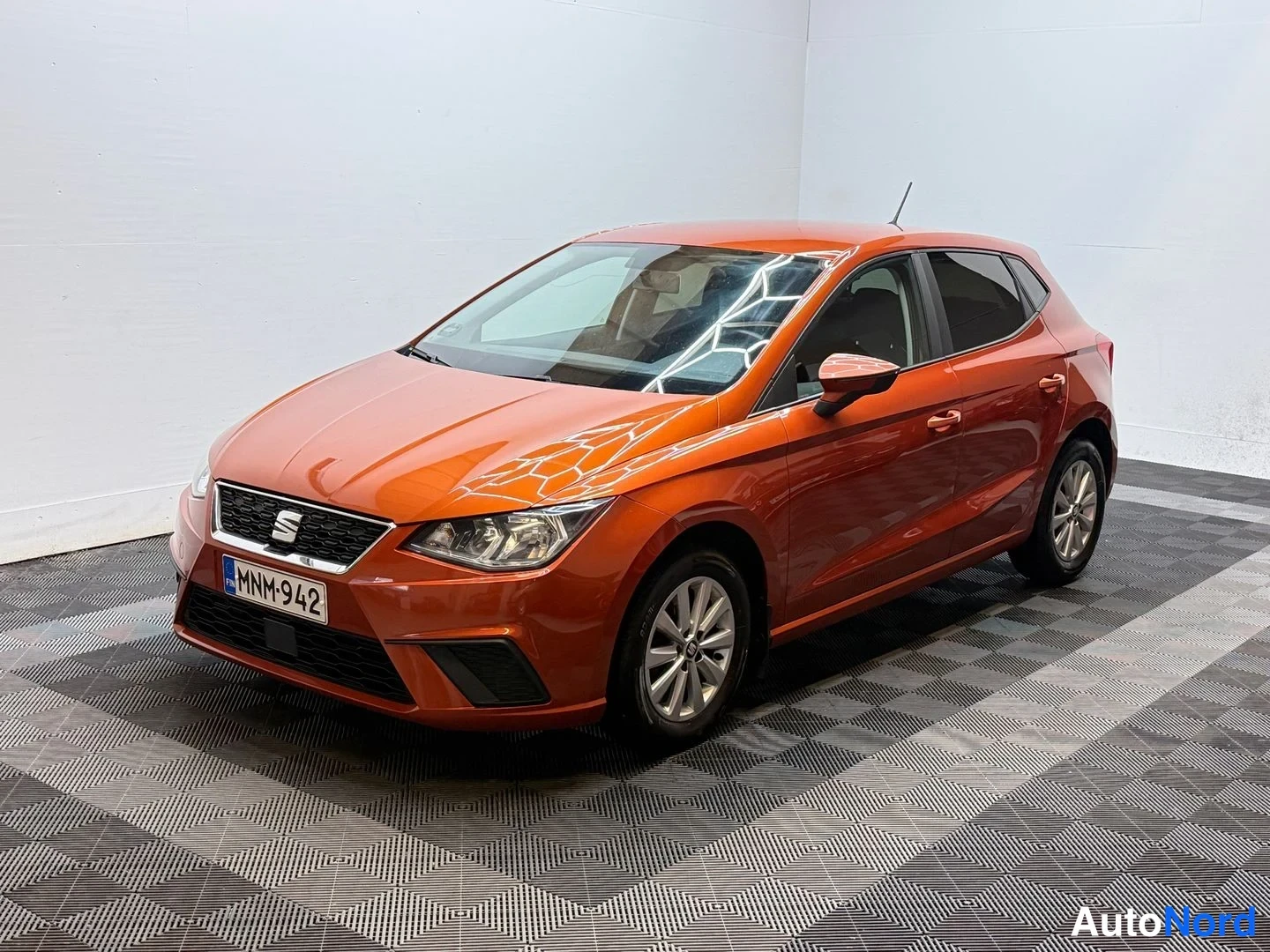 Etuviisto, nokka vasemmalle: Oranssi Seat Ibiza -henkilöauto kuvattu etukulmasta sisätilassa, rekisterikilpi.