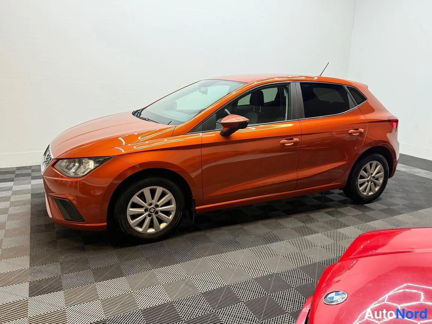 Etuviisto, nokka vasemmalle: Oranssi Seat Ibiza etuvasalta sivulta hallissa.