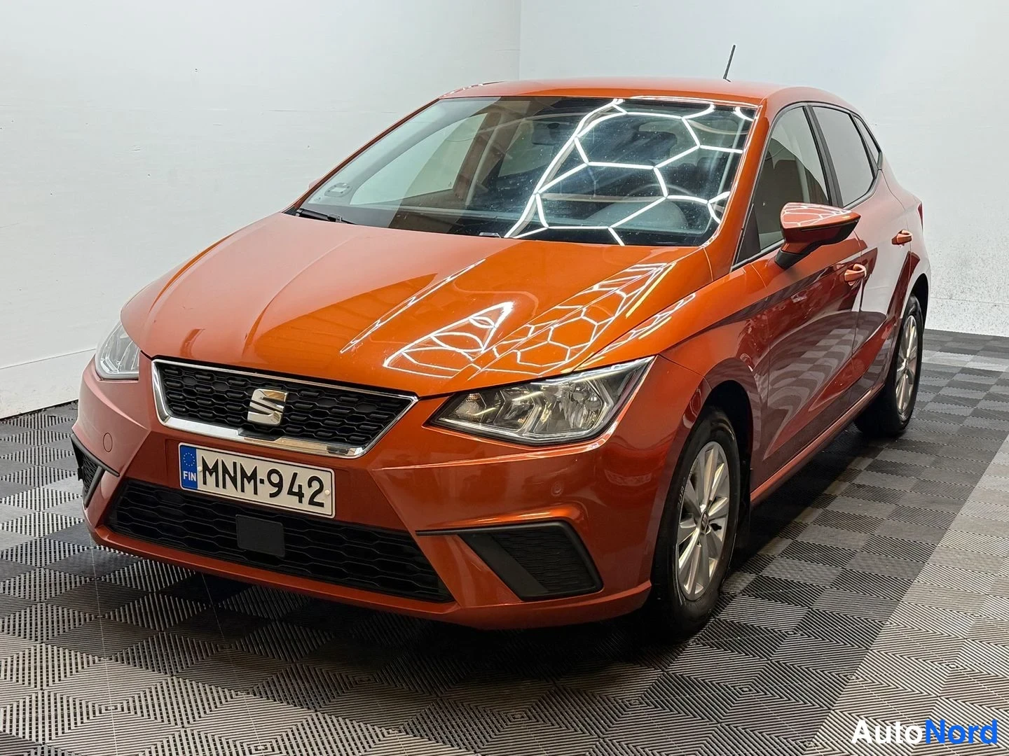 Etuviisto, nokka vasemmalle: Oranssi Seat Ibiza etukulmasta sisätilassa, rekisterikilpi, SEAT-merkki etusäleikössä.