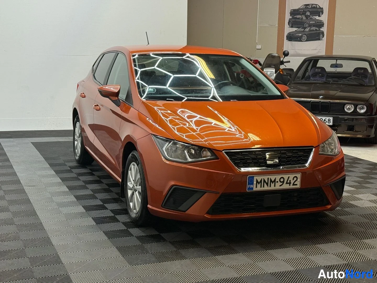 Etuviisto, nokka oikealle: Kokonaisuudessaan oranssi Seat Ibiza viistosti edestä oikealta sisähallissa, rekisterikilpi.