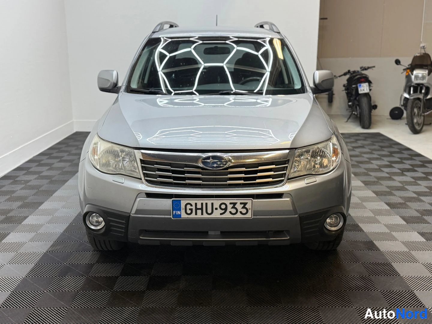 Edestä: Etukulmasta kuvattu hopeanharmaa Subaru Forester, etusälekaita, sumuvalot ja rekisterikilpi.