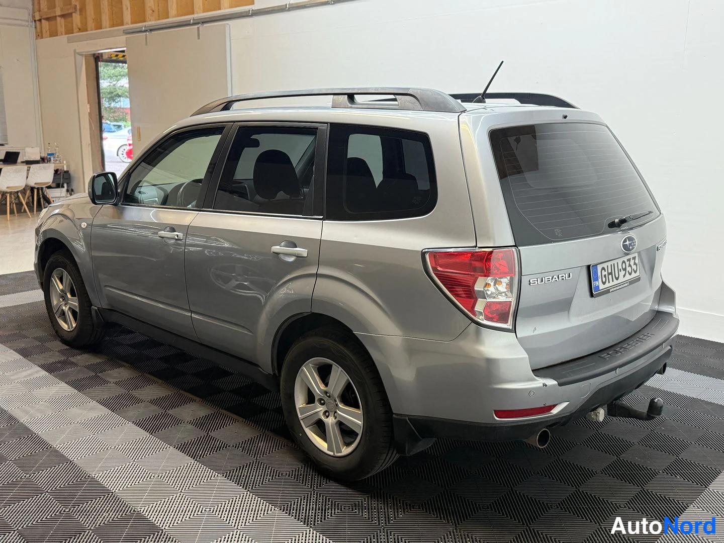 Takaviisto: Hopeanharmaa Subaru Forester takaa vasemmalta sivulta kuvattuna; rekisteritunnus, kattokaiteet ja vetokoukku näkyvissä.