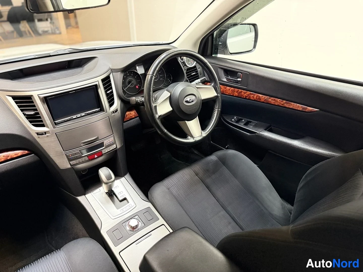 Edestä: Auton sisätilat: ohjaamo, Subaru-ohjauspyörä, kosketusnäyttö, automaattivaihdevipu ja kangasistuimet.