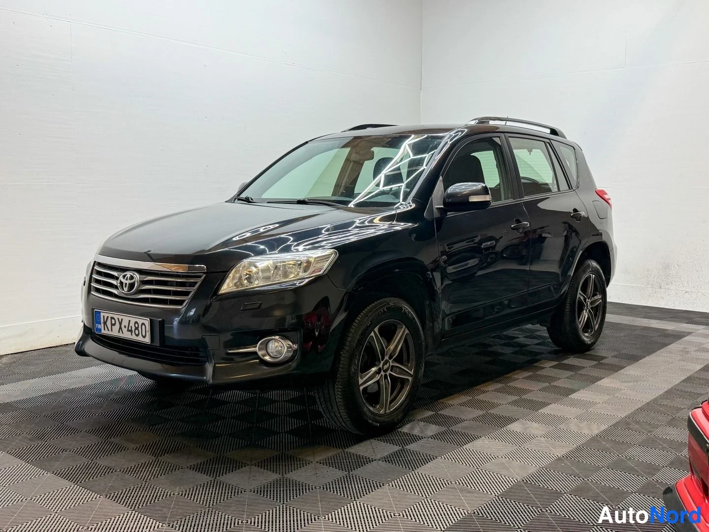 Etuviisto, nokka vasemmalle: Toyota RAV4 musta, etukulma vasemmalta, rekisterikilpi, kaiteet katolla.