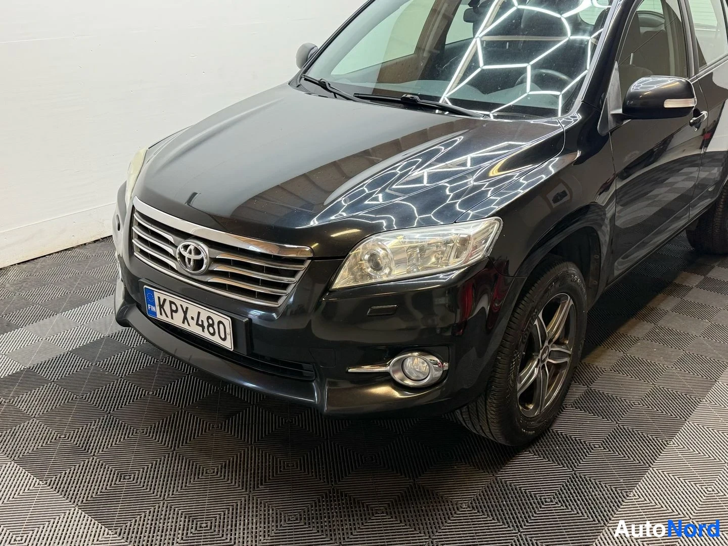 Etuviisto, nokka vasemmalle: Mustan Toyota RAV4:n etukolmivuoressa näkyy etusäleikkö, Toyota-merkki, ajovalot ja rekisterikilpi.