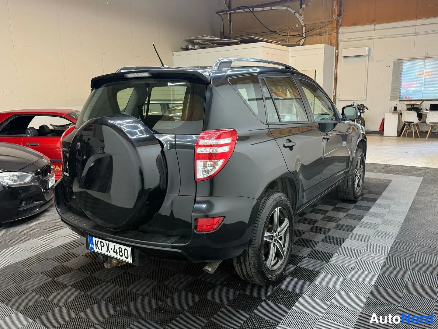 Takaviisto: Mustan Toyota RAV4:n takakolmivuores näkyy varapyörä, takavalo, kattokaaret ja rekisterikilpi.