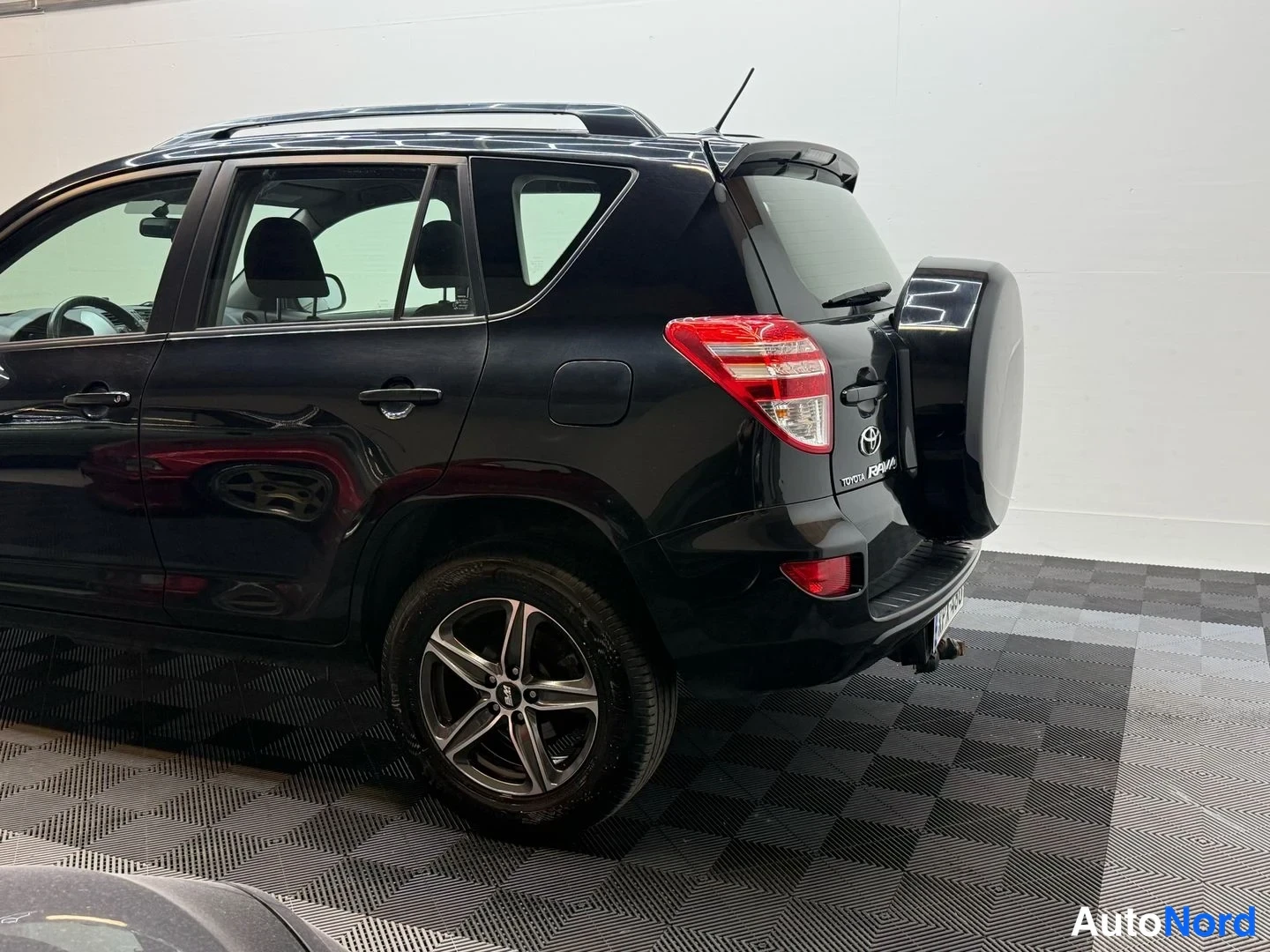 Takaviisto: Mustan Toyota RAV4:n takakulma sivulta, varapyörä ja perävaunun kytkin näkyvät.