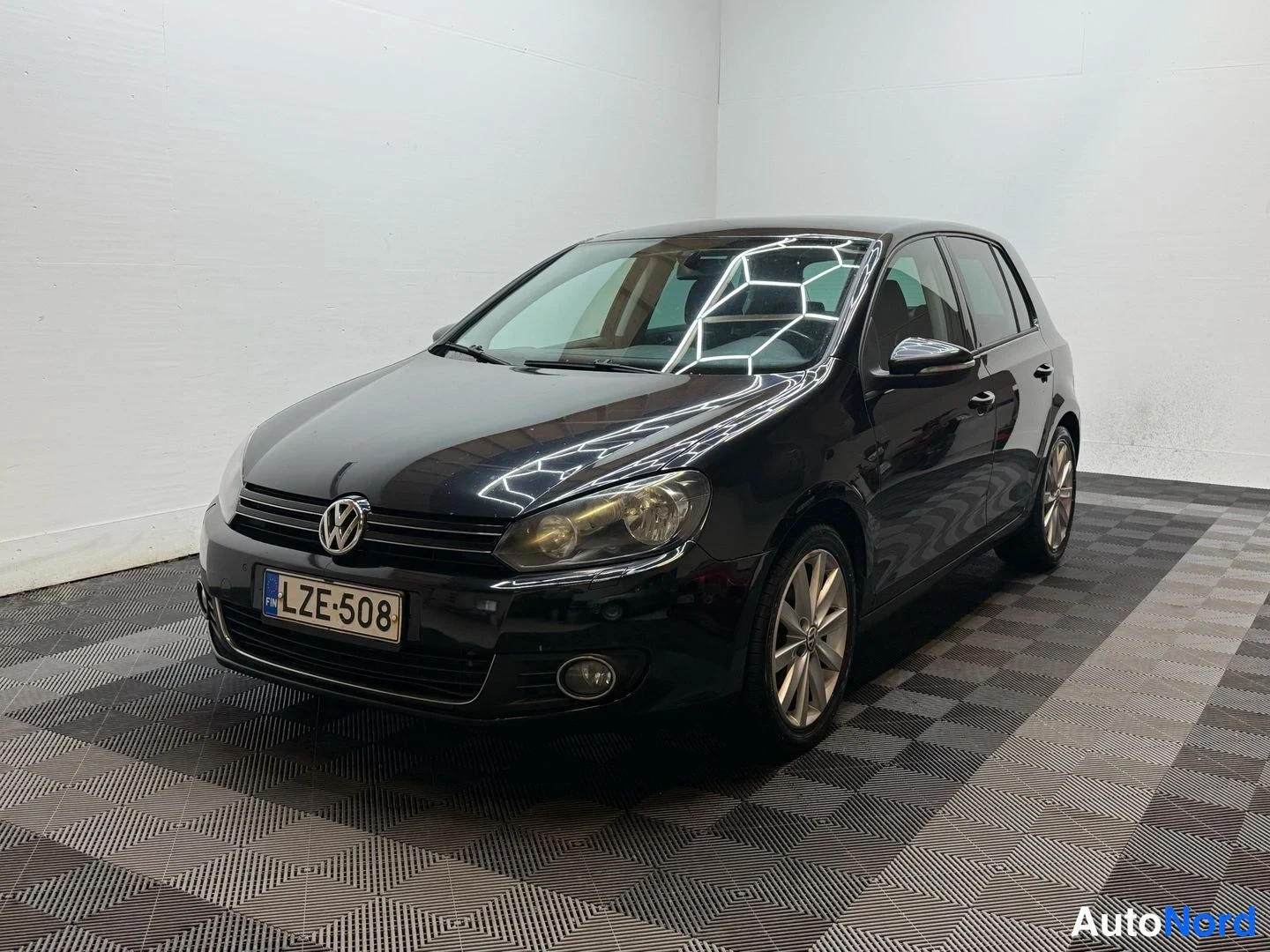 Etuviisto, nokka vasemmalle: Mustan Volkswagen Golfin etukulmakuva vasemmasta etukulmasta, rekisterikilpi.
