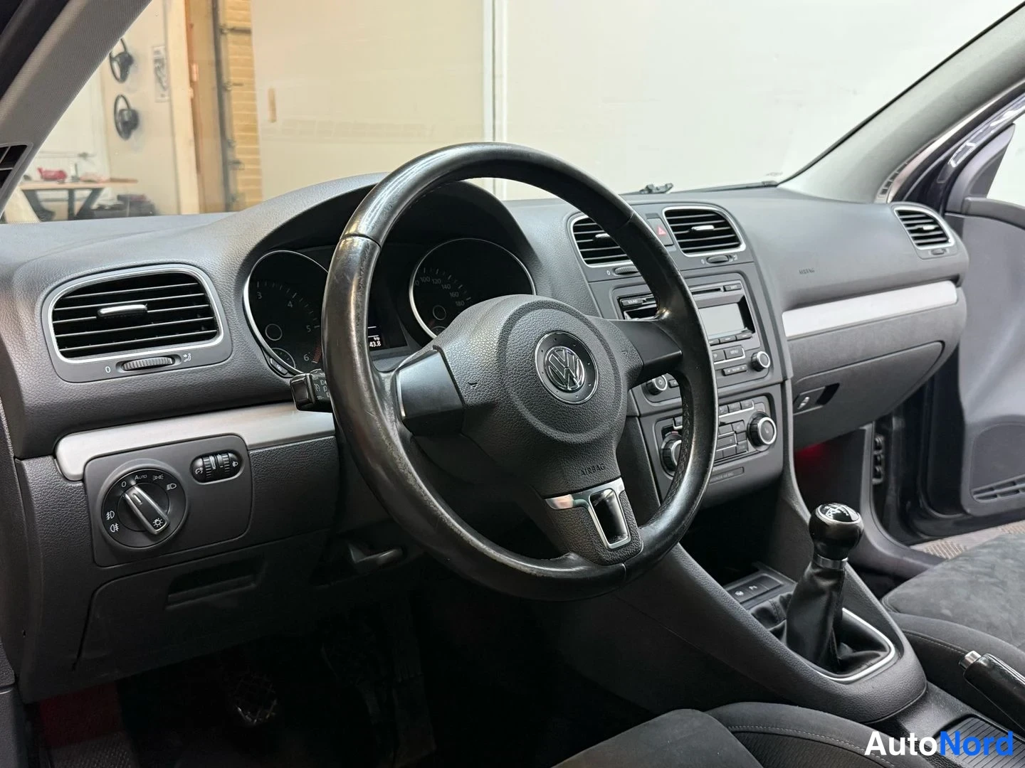 Muu: Volkswagenin ohjaamo: tuplakestot, VW-logo, radio ja manuaalivaihteisto näkyvät kojelaudalla.