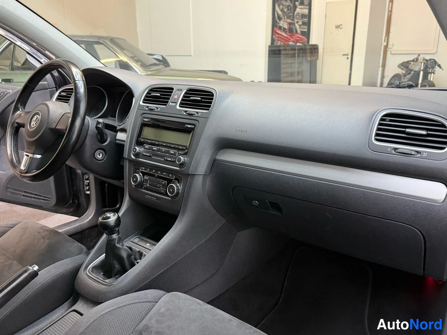 Muu: Auton kojelauta ja ristinpuinen vaihtajanippi; näkyvissä radio, ilmastointiautot ja Volkswagen-merkitty ohjauspyörä.