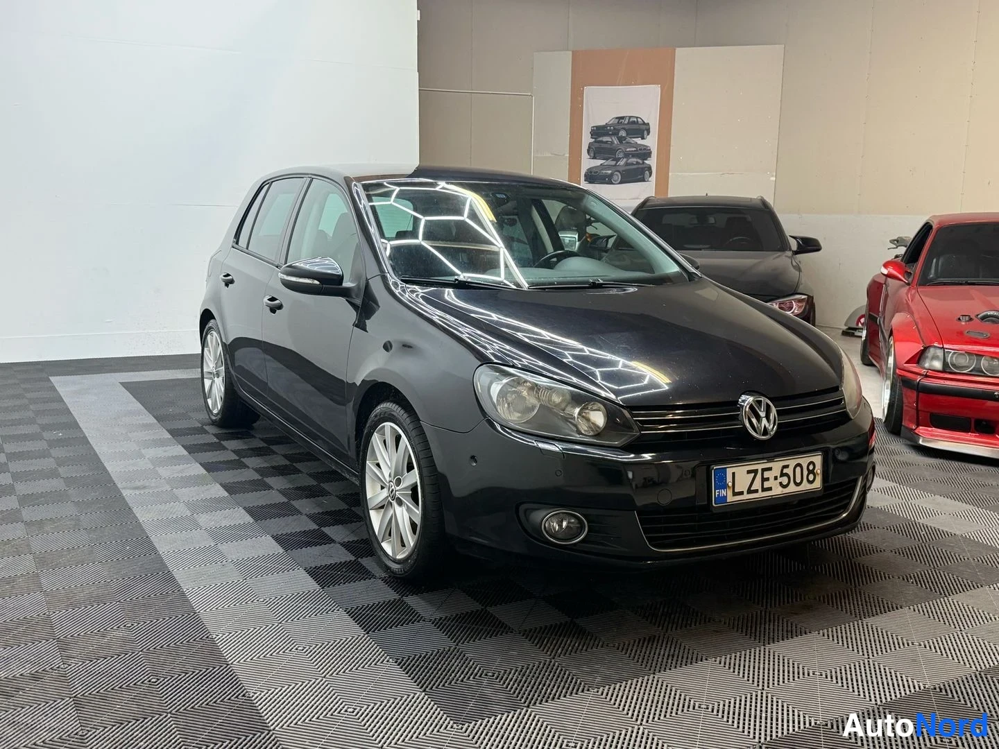 Etuviisto, nokka oikealle: Mustan Volkswagen Golfin etukulmakuva oikeasta etukulmasta, rekisterikilpi.