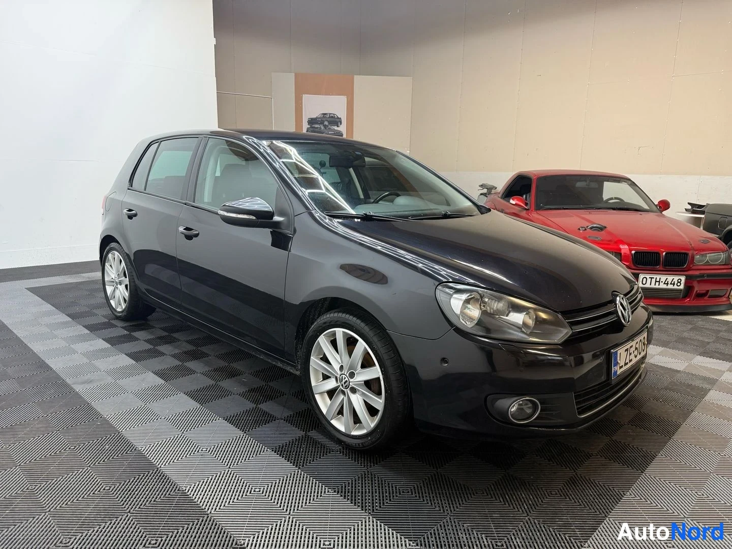 Etuviisto, nokka oikealle: Mustan Volkswagen Golfin etukulmatarkastus sisätilassa, kylki ja etusäiliö näkyvät.