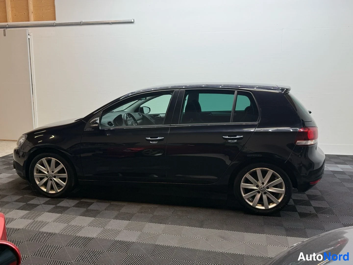 Sivulta: Volkswagen Golfin täysi sivukuva vasemmalta, päänäkökulmassa, musta, kevytmetallivanteet ja tummat lasit.