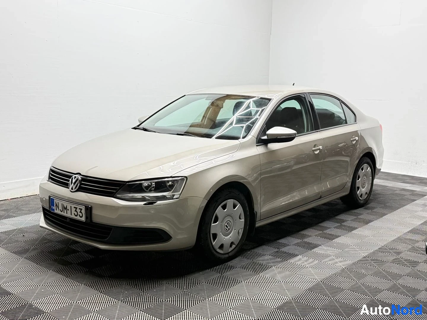 Etuviisto, nokka vasemmalle: Volkswagen Jetta -sedanin etukulmanäkymä, vaaleanbeige koripaneelit ja rekisterikilpi.