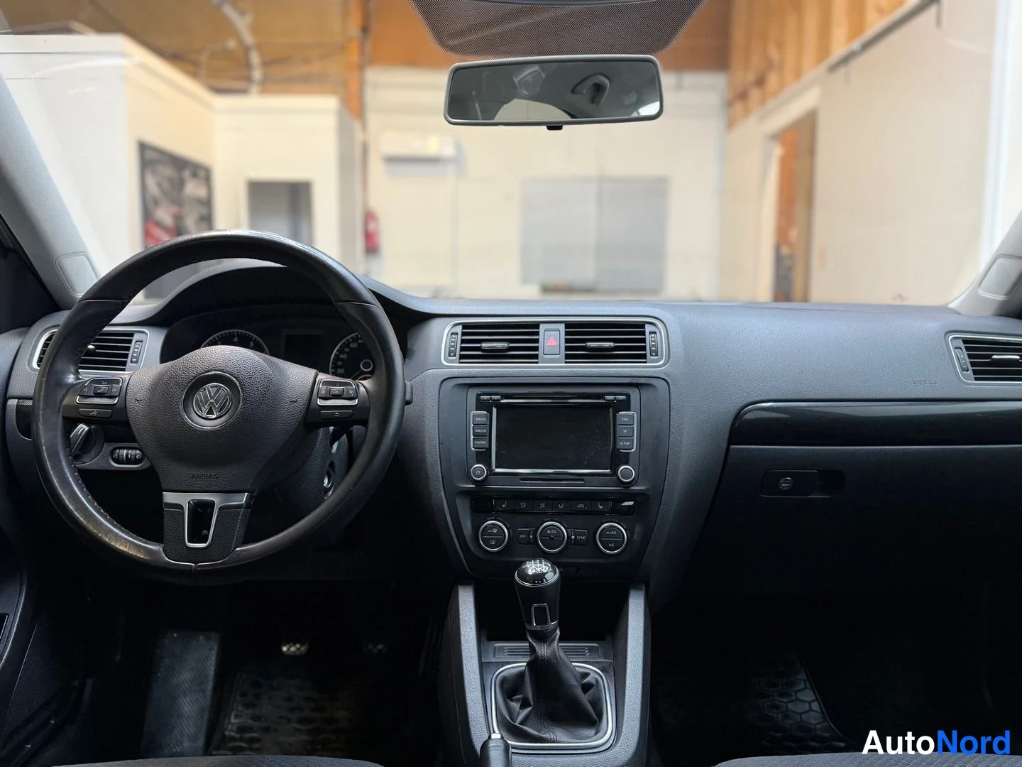 Edestä: Ohjaamo näkyvissä: Volkswagen-ohjauspyörä, manuaalivaihteisto, radio ja tumma kojelauta.