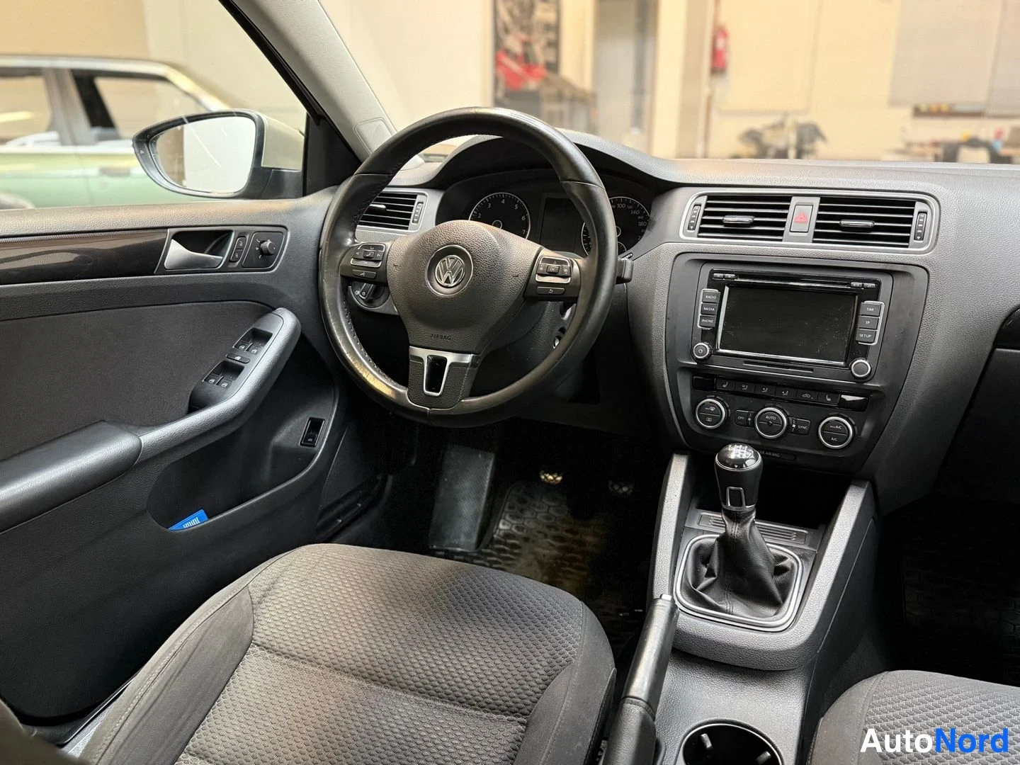 Edestä: Kuljettajan puolen näkymä: Volkswagen-ohjauspyörä, ikkunakytkimet ovessa, manuaalivaihto ja radio.