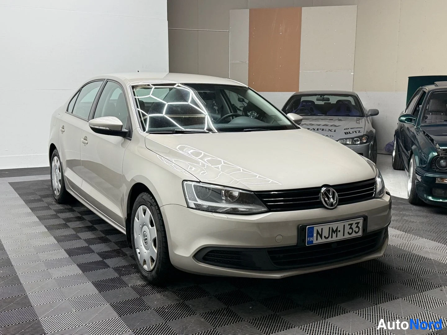 Etuviisto, nokka oikealle: Volkswagen Jetta -sedanin etukulma kuvattuna oikealta, vaalean kermanvärinen runko ja tumma etusäleikkö rekisterikilvellä.