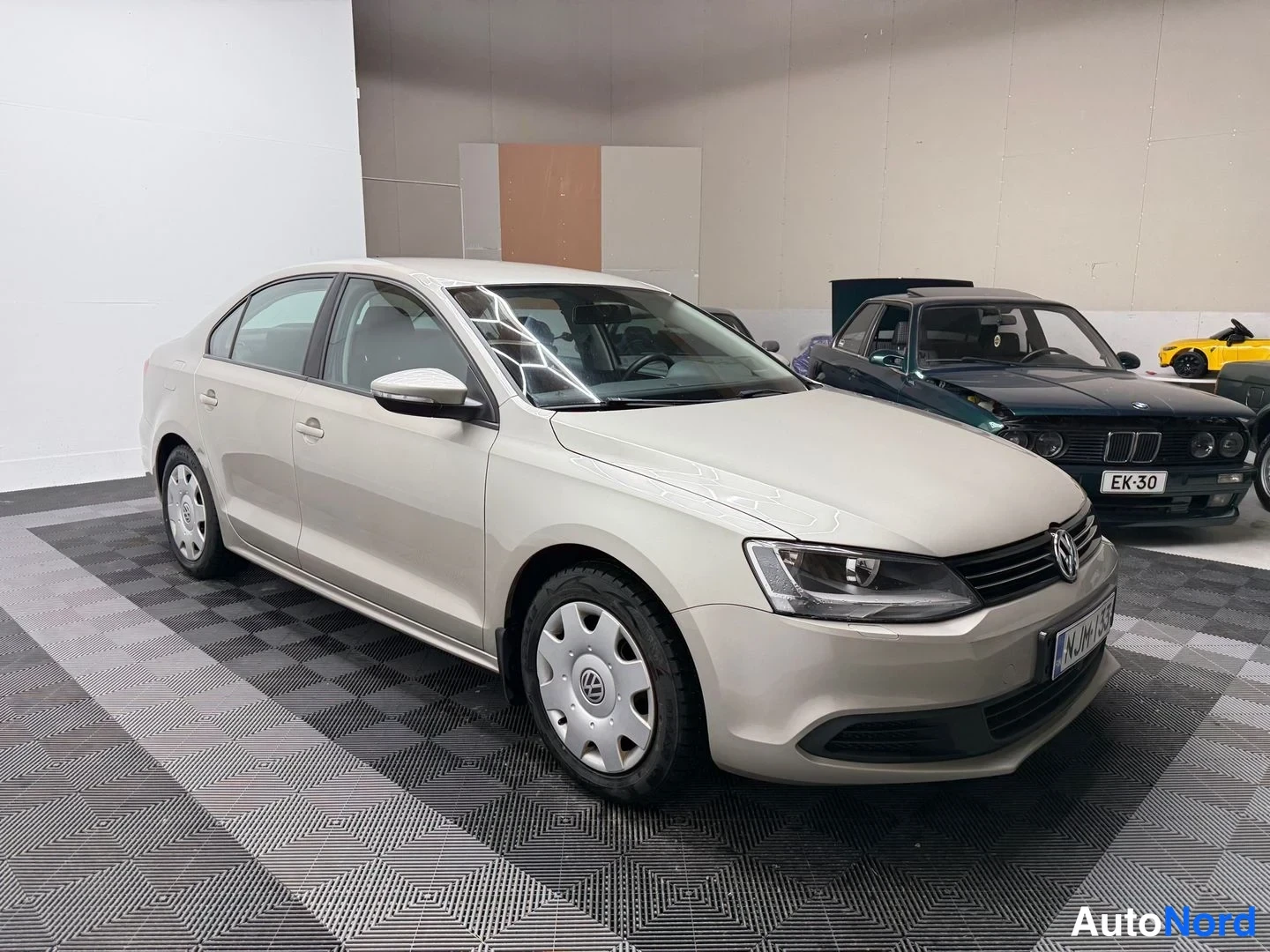Etuviisto, nokka oikealle: Volkswagen Jetta -sedanin etukulma kuvattuna oikealta, vaalean kermanvärinen runko, teräsvannet ja rekisterikilpi osittain näkyvissä.