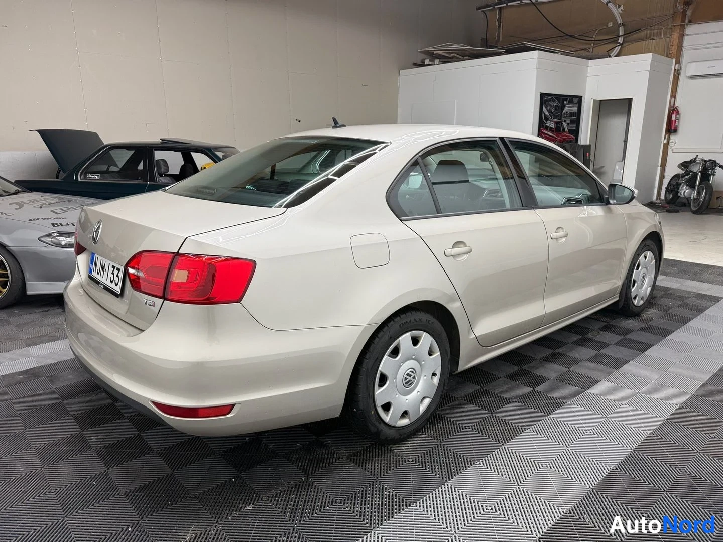 Takaviisto: Volkswagen Jetta -sedanin takakulma kuvattuna vasemmalta, vaalean kermanvärinen runko, punaiset takavalot ja rekisterikilpi.