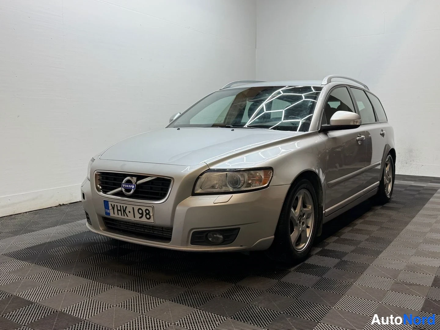 Etuviisto, nokka vasemmalle: Hopeinen Volvo V50 -farmari etuviistosta sisätilassa, rekisterikilpi.