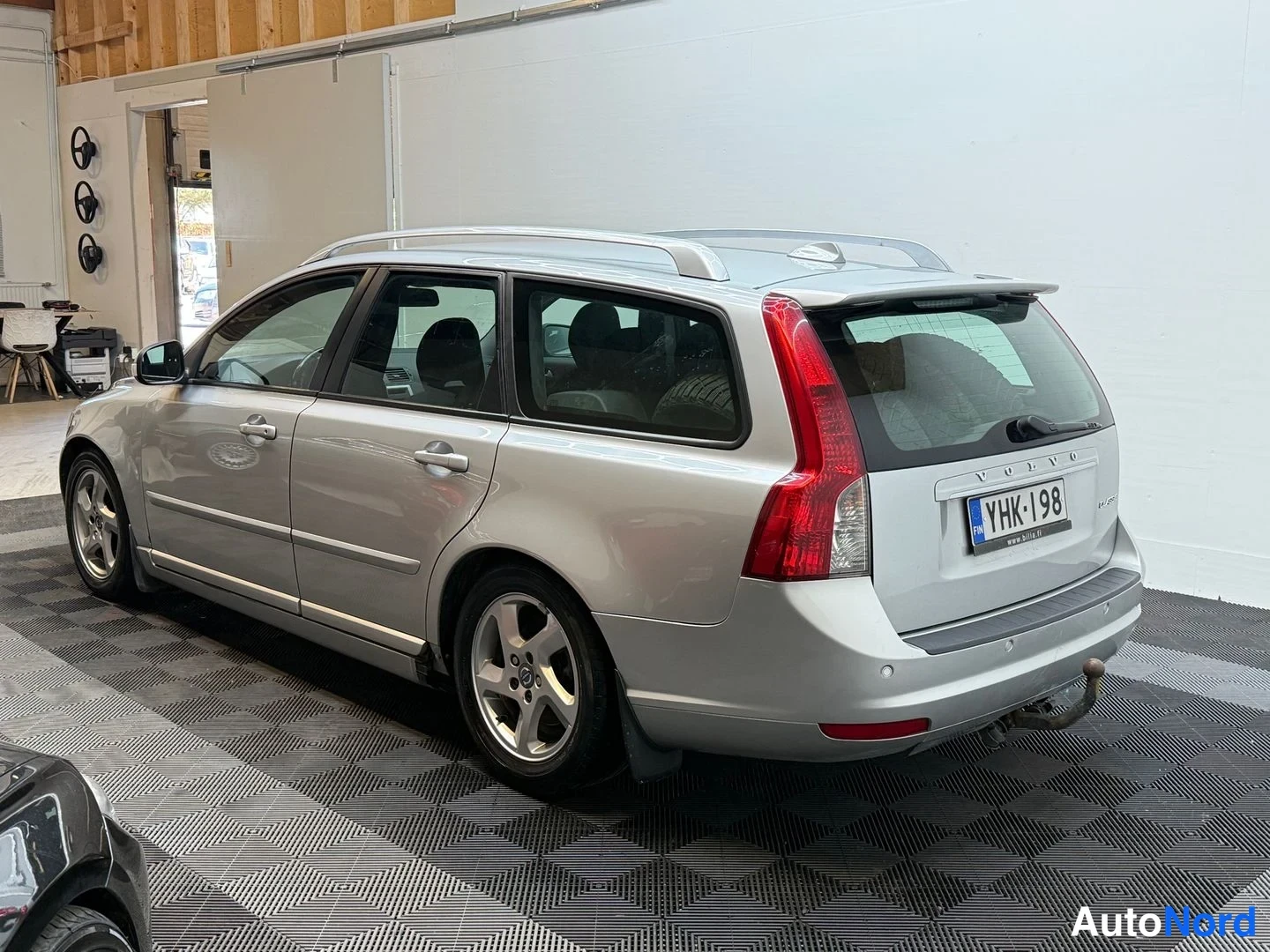 Takaviisto: Hopeanharmaa farmariauto takaapäin ja oikealta sivulla hallissa, koko auto näkyy, rekisterikilpi, vetokoukku takana.