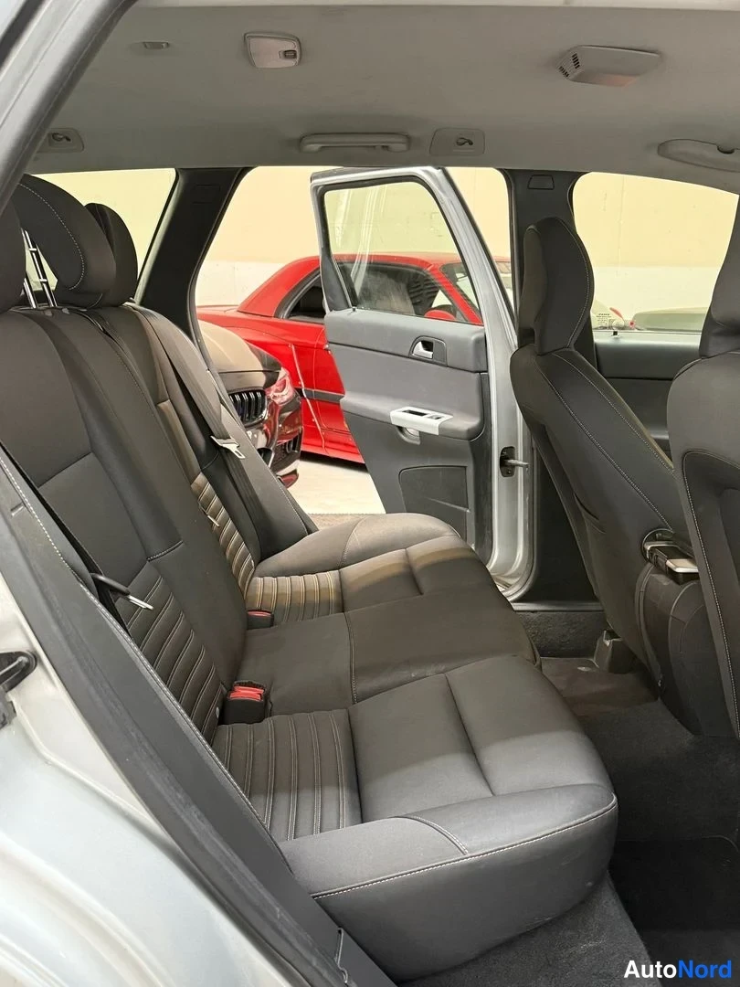 Muu: Takapenkin sisätila takaa käsin kuvattuna: tummat penkkiosat ja selkänojat, kuljettajan puolen ovi auki, taustalla punainen auto.