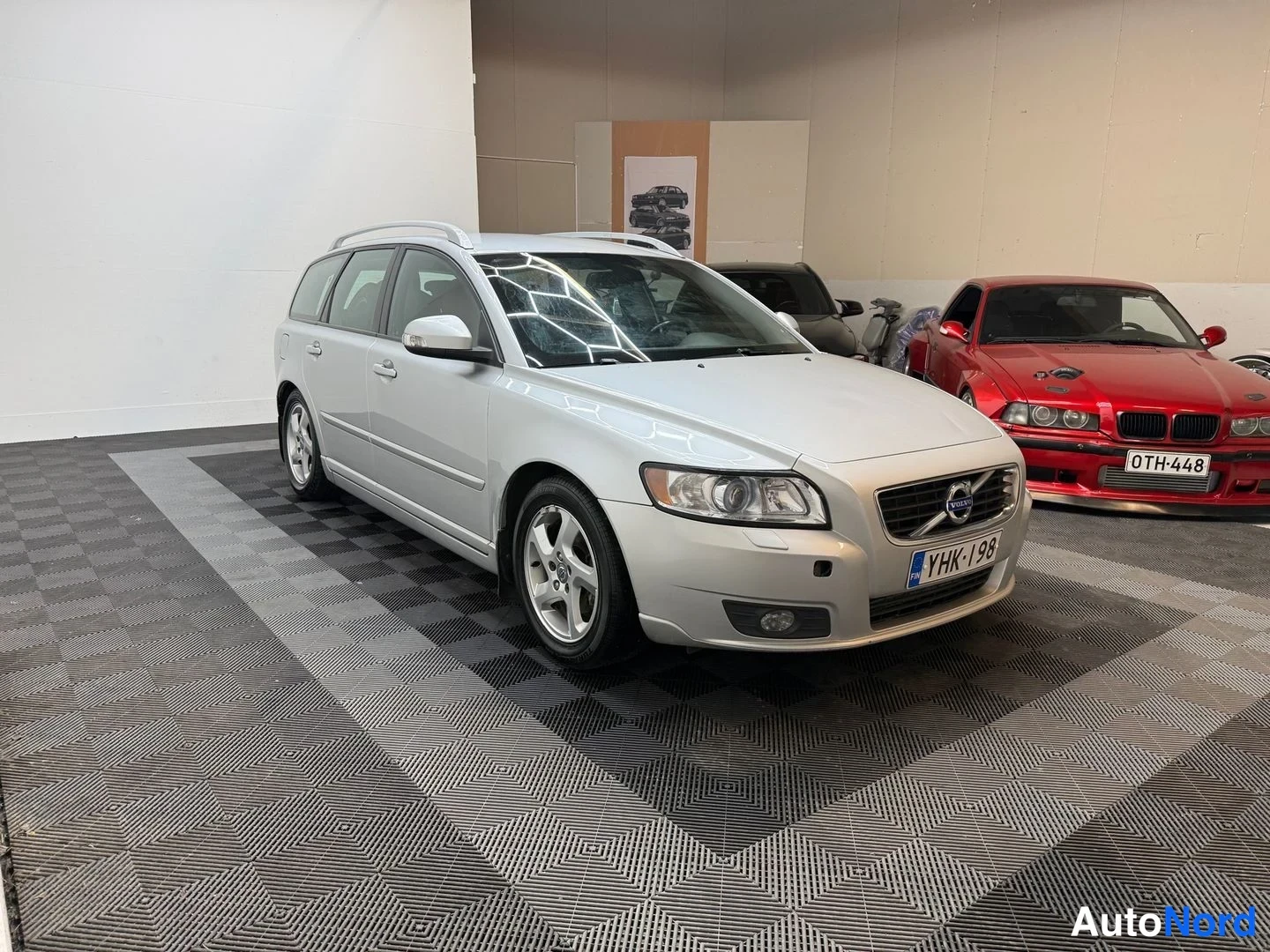 Etuviisto, nokka oikealle: Hopeanharmaa Volvo V50 -farmari etuviistosta oikealta sisätiloissa, kylki ja keula näkyvissä, rekisterikilpi.