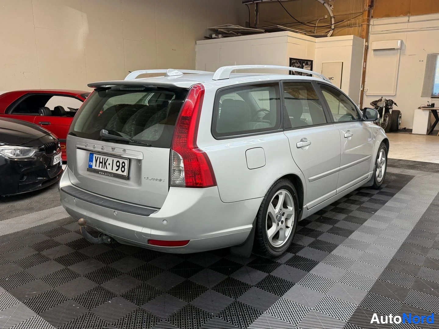 Takaviisto: Hopeanharmaa Volvo V50 -farmari takaviistosta vasemmalta sisätiloissa, takavalot ja rekisterikilpi näkyvissä.