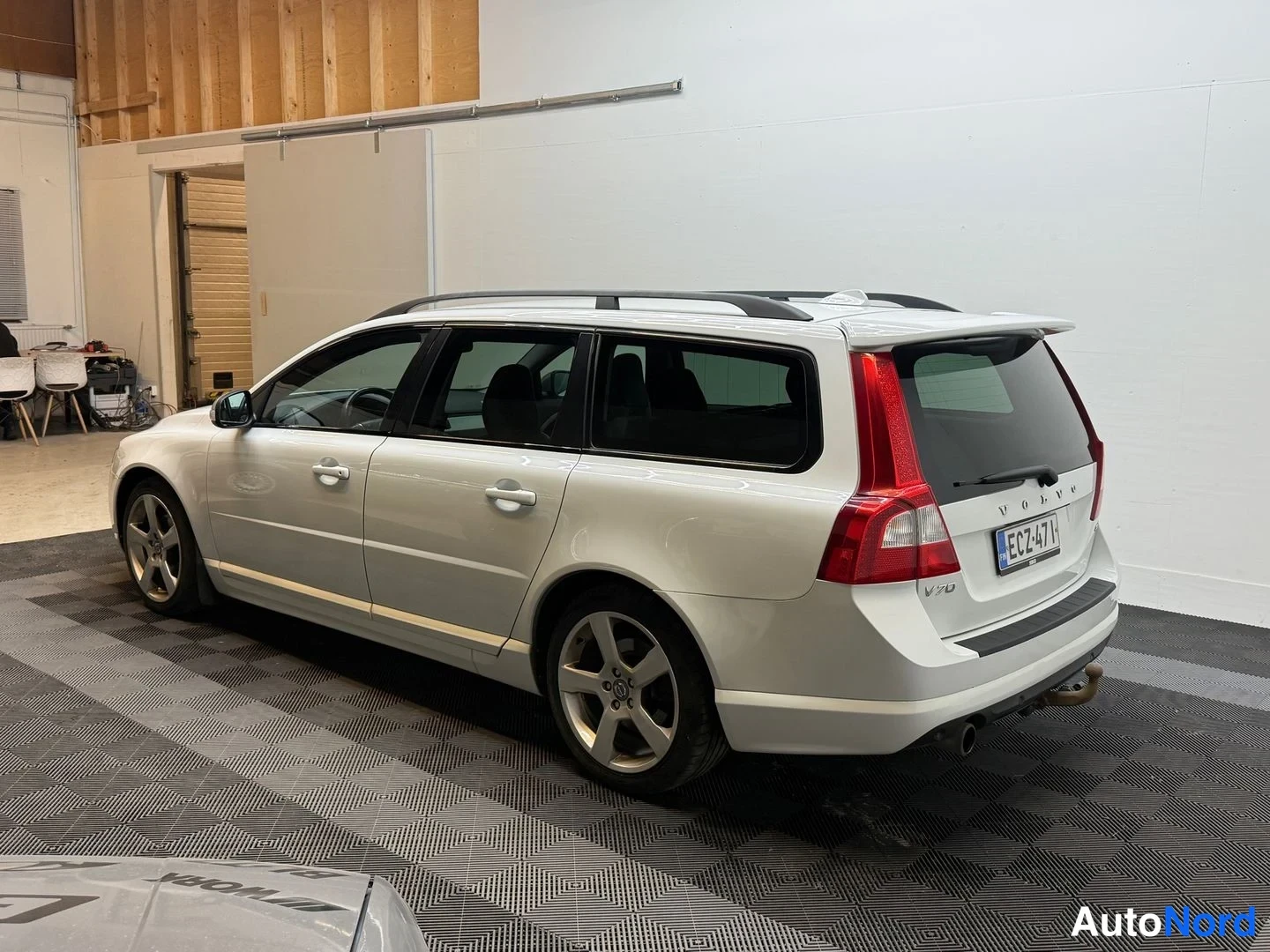 Takaviisto: Valkoinen Volvo V70 -farmari takaviistosta oikealta nähtynä: kattokaiteet, kevytmetallivanteet, rekisterikilpi ja V70-merkintä näkyvät; auton runko on valkoinen