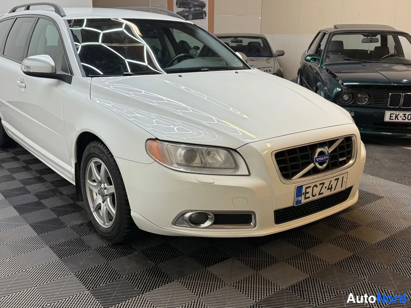 Etuviisto, nokka oikealle: Valkoisen Volvo V70 -farmarin kolmeneljäsosan etunäkymä vasemmasta kyljestä, kylpeili ja -rekisterikilpi näkyvissä.