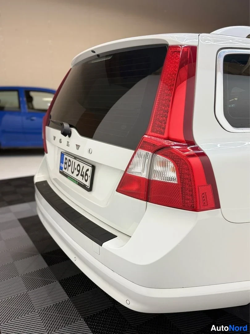 Takaviisto: Valkoisen farmarin takakulma: VOLVO-teksti, punaiset takavalot ja rekisterikilpi.
