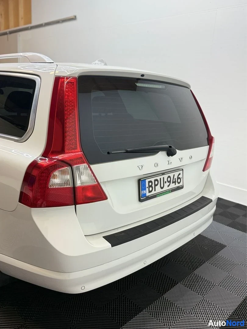 Takaviisto: Auton takaosan kolmeneljännesnäkymä: valkoinen farmarikorinen Volvo, takana punaiset takavalot ja rekisterikilpi.